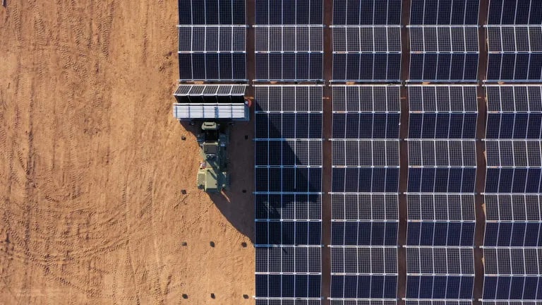 Aerial view of a solar panel installation in a desert area with a vehicle transporting additional panels.